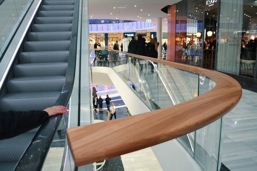Buet overligger i klarlakkert eik langs glassrekkverket i Mall of Scandinavia
