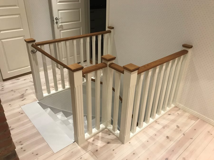 Hvitt rekkverk med håndløper i tre rundt en trappeåpning